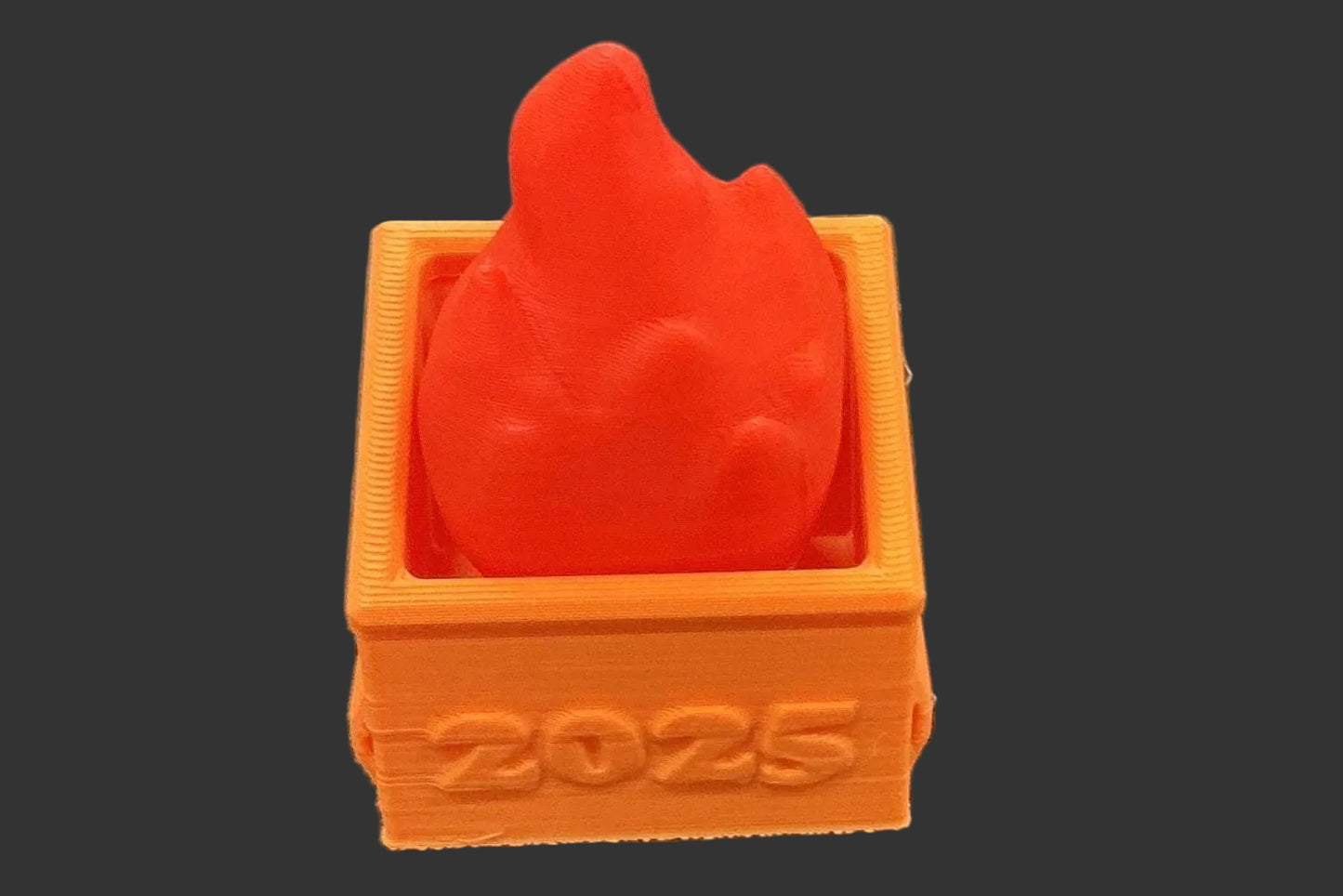 Red heart-shaped object inside an orange box with '2025' printed on it, on a gray background